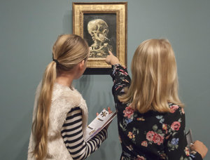 Twee blonde meisjes met een checklist bij Van Goghs schilderij 'Kop van een skelet met brandende sigaret'. Het rechtermeisje wijst naar het schilderij. Foto: Les Adu